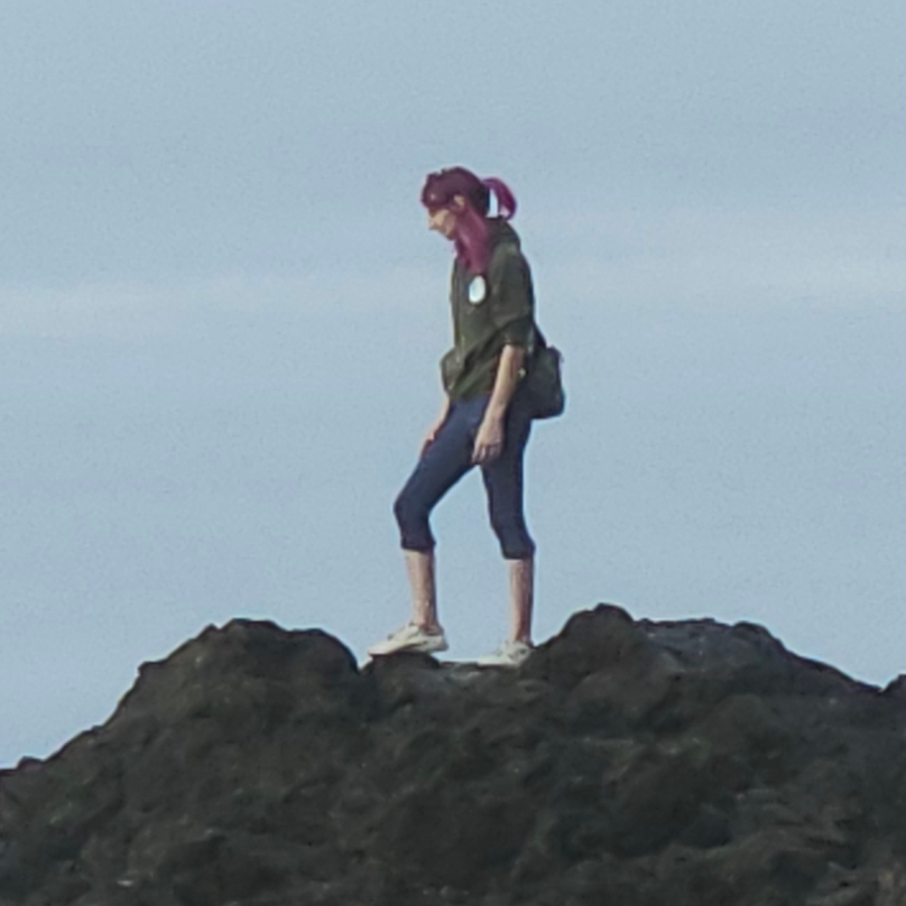 a pink haired woman stands on a rock formation